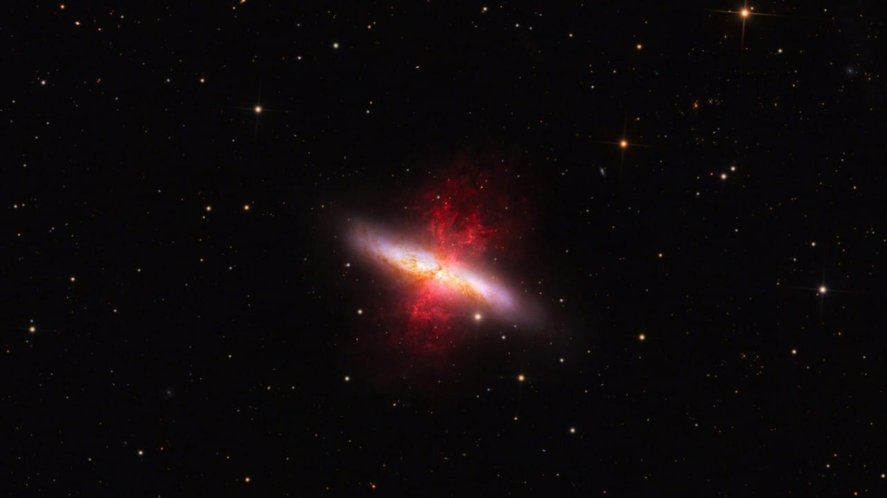 Imagini astrale ale Galaxiei Trabuc (M82), evidențiind discul său albastru și plumele de hidrogen ionizat ce ies din nucleu, înconjurată de stele și galaxii din fundal.